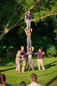 Shena stands on top of two other acrobats shoulders