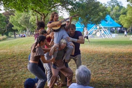 Mandolin player dismounting from a bunch of acrobats