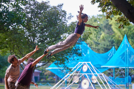 Acrobat flying through the air in front of outdoor artwork