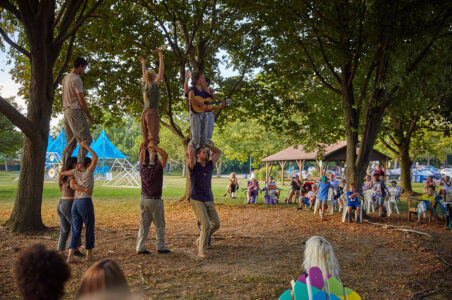 Acrobat playing mandolin that is standing on the shoulders of another acrobat